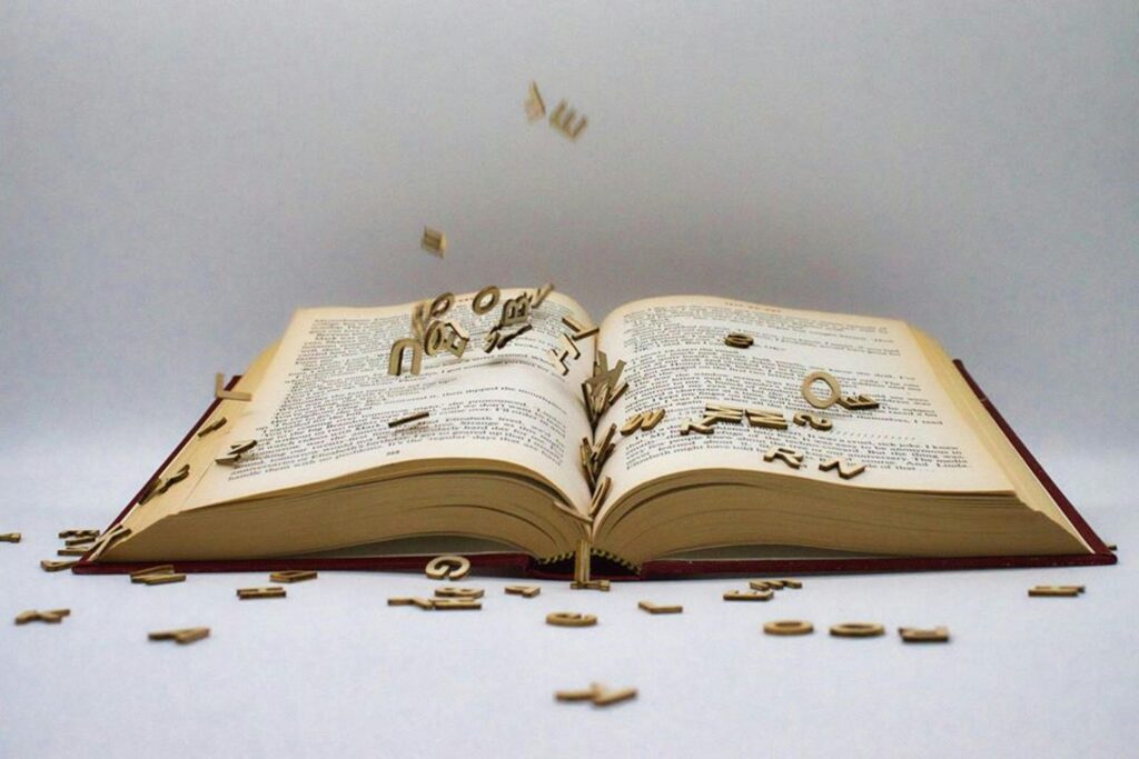 An open book with scattered wooden letters creating a surreal scene.