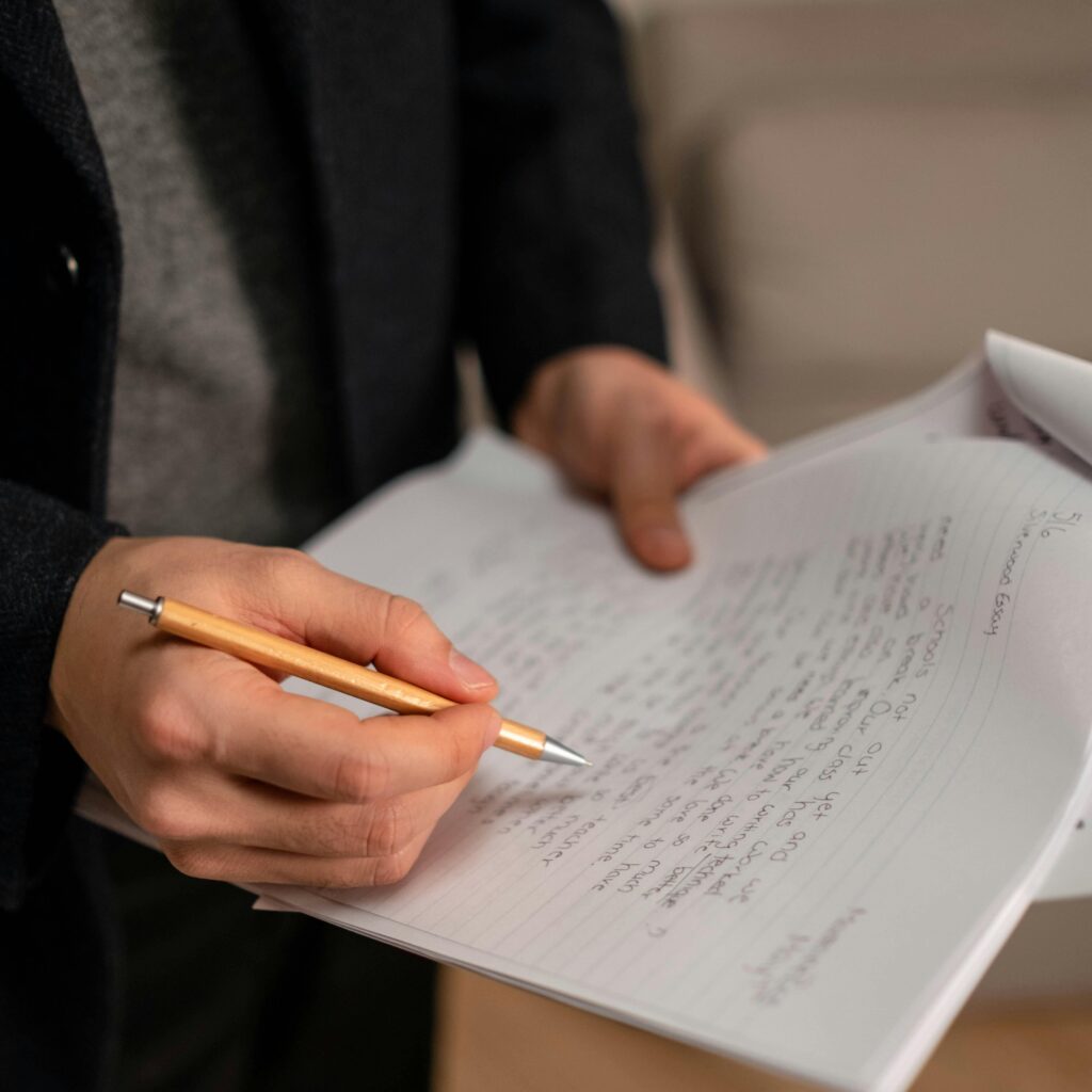 Close-up of a person holding a pen and writing notes on paper indoors.